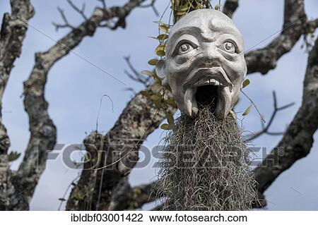 Stock Image - "A mask hanging on a tree, at the Wat Rong Khun temple or The White Wat, a Buddhist-Hindu temple, Chiang Rai, Chiang Rai Province, Northern Thailand, Thailand, Asia". Fotosearch
