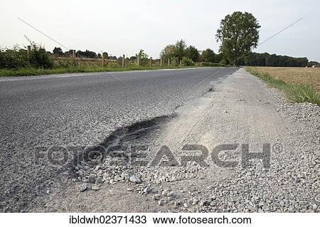 Stock Image - "A road with an unpaved shoulder and a road hole, Dortmund, Ruhr area, North Rhine-Westphalia, Germany, Europe, PublicGround, Europe". Fotosearch