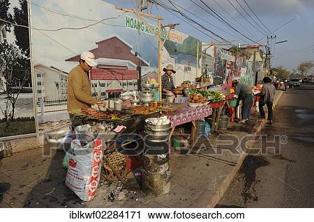 Stock Image - "A row of food stalls in front of Vietnamese billboards, advertisement poster with projects under the name of the Vietnamese soccer club Hoang Anh Gia Lai in Laos, Vientiane, Laos, Southeast Asia, Asia". Fotosearch