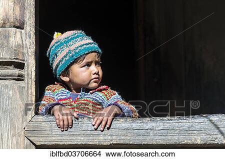 Picture - "A small child looking out of the window of a wooden house, Chitkul, Himachal Pradesh, India, Asia". Fotosearch