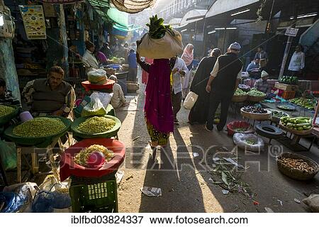 Stock Photo - "A woman is carrying a bag with vegetables on her head through the vegetable market, Ahmedabad, Gujarat, India, Asia". Fotosearch