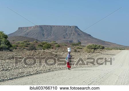 "A woman with a bucket on her head standing at a gravel road in dry landscape, Kunene Region, Namibia, Africa" View Large Photo Image Stock Image - "A woman with a bucket on her head standing at a gravel road in dry landscape, Kunene Region, Namibia, Africa". Fotosearch
