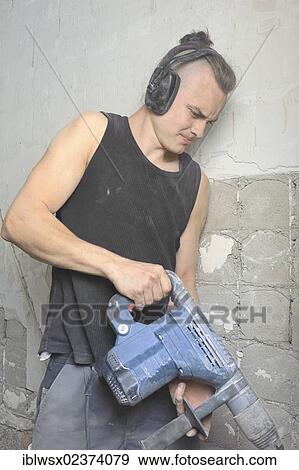 Stock Photo - "A young man with partly shaved head using with a drill hammer, refurbishment, Baden-Wuerttemberg, Germany, Europe". Fotosearch