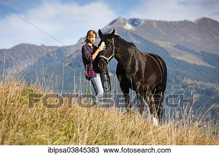 "A young woman and a black Hanoverian horse standing on a mountain meadow in autumn, North Tyrol, Austria, Europe" View Large Photo Image Stock Image - "A young woman and a black Hanoverian horse standing on a mountain meadow in autumn, North Tyrol, Austria, Europe". Fotosearch