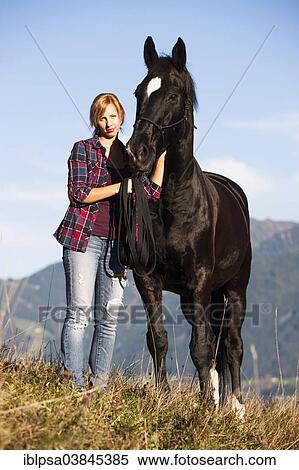 "A young woman and a black Hanoverian horse standing on a mountain meadow in autumn, North Tyrol, Austria, Europe" View Large Photo Image Stock Photography - "A young woman and a black Hanoverian horse standing on a mountain meadow in autumn, North Tyrol, Austria, Europe". Fotosearch