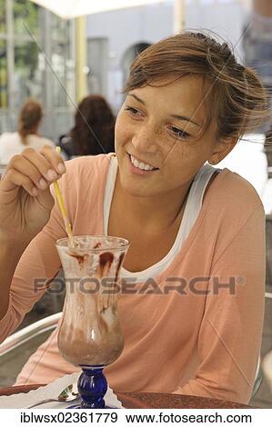 Stock Photo - "A young woman of Indonesian descent sitting in a street cafe drinking an iced coffee, Baden-Wuerttemberg, Germany, Europe, PublicGround, Europe". Fotosearch