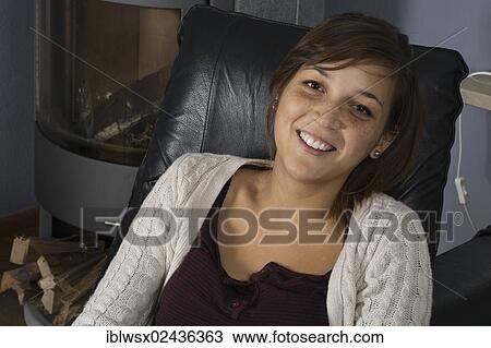 "A young woman of Indonesian origin is sitting on a leather armchair in front of a wood burner, relaxing, Germany, Europe" View Large Photo Image Stock Image - "A young woman of Indonesian origin is sitting on a leather armchair in front of a wood burner, relaxing, Germany, Europe". Fotosearch