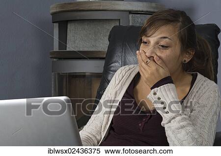 Stock Photography - "A young woman of Indonesian origin is sitting in front of a wood burner working on a laptop computer, Germany, Europe". Fotosearch