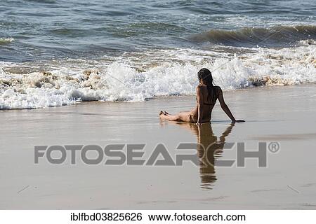 Stock Photograph - "A young woman wearing bikini is sitting in the sand of Anjuna Beach, Anjuna, Goa, India, Asia". Fotosearch