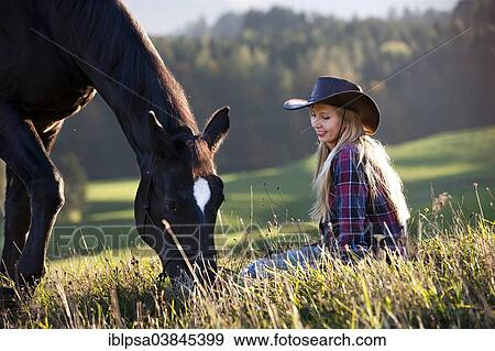 Stock Photo - "A young woman with a black Hanoverian horse on a mountain meadow in autumn, North Tyrol, Austria, Europe". Fotosearch