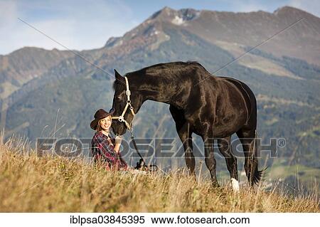 Stock Photography - "A young woman with a black Hanoverian horse on a mountain meadow in autumn, North Tyrol, Austria, Europe". Fotosearch
