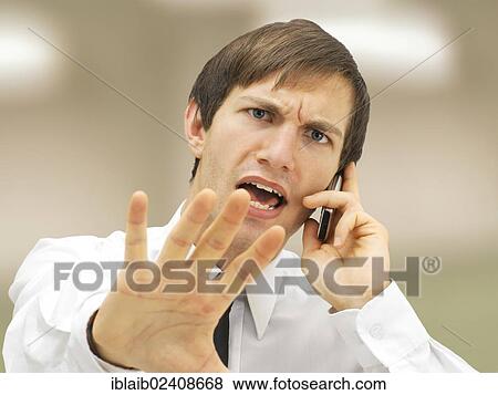 Stock Photo - "Aggressive businessman speaking on his mobile phone, portrait, stressed, defensive gesture". Fotosearch