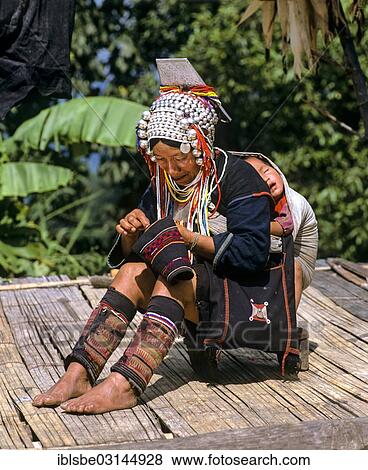 Stock Photo - "Akha woman in a mountain village, in traditional costume and headdress with silver bells, child sleeping in a sling on her back, Chiang Rai Province, Northern Thailand, Thailand, Asia". Fotosearch