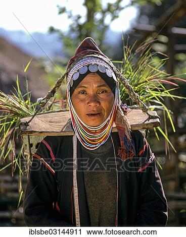 Stock Image - "Akha woman in traditional costume and headdress with silver coins, with a pannier, in a mountain village, Chiang Rai Province, Northern Thailand, Thailand, Asia". Fotosearch
