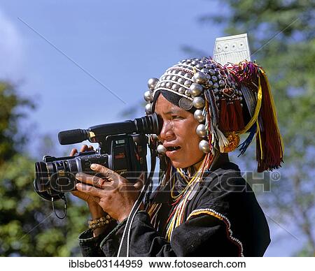 Stock Photo - "Akha woman in traditional costume and headdress with silver bells, operating a Canovision A1 Hi8 video camera, Chiang Rai Province, Northern Thailand, Thailand, Asia". Fotosearch