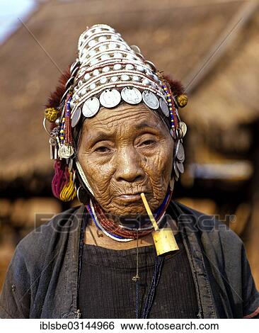 Stock Photograph - "Akha woman with a pipe, a traditional dress and headdress with silver coins, portrait, Chiang Rai Province, Northern Thailand, Thailand, Asia". Fotosearch