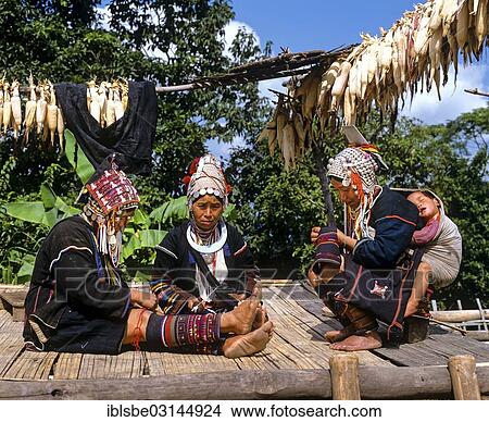 Picture - "Akha women in a mountain village, in traditional costume and headdresses with silver coins, one carrying a sleeping child in a sling on her back, Chiang Rai Province, Northern Thailand, Thailand, Asia". Fotosearch