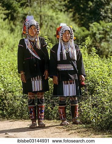 Stock Image - "Akha women in a mountain village, in traditional costume and headdress, Chiang Rai Province, Northern Thailand, Thailand, Asia". Fotosearch