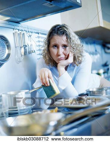 Annoyed woman holding a sponge while standing in a kitchen with dirty dishes View Large Photo Image Stock Image - Annoyed woman holding a sponge while standing in a kitchen with dirty dishes. Fotosearch
