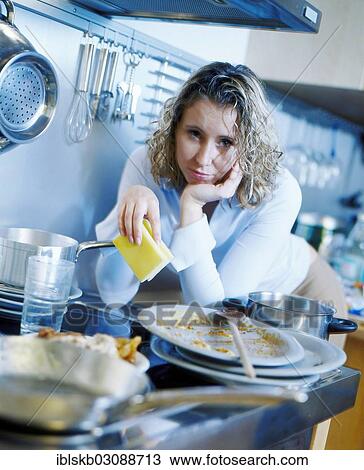 Annoyed woman holding a sponge while standing in a kitchen with dirty dishes View Large Photo Image Stock Image - Annoyed woman holding a sponge while standing in a kitchen with dirty dishes. Fotosearch