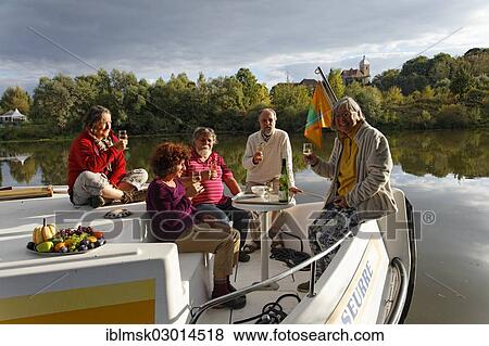 Stock Photo - "Aperitif in the evening sun, on the bow terrace of a Penichette, a houseboat on the Saone River in a quiet tributary, in the Saone Valley Marina, Traves, Vesoul, Region Franche-Comte, Dep. Haute-Saone, France, Europe". Fotosearch