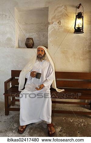 Arab wearing a traditional white dishdasha robe sitting on a bench with a cup of water, life-size figure, Al-Ahmadiya School Museum, Dubai, United Arab Emirates, Middle East, Asia View Large Photo Image Stock Image - Arab wearing a traditional white dishdasha robe sitting on a bench with a cup of water, life-size figure, Al-Ahmadiya School Museum, Dubai, United Arab Emirates, Middle East, Asia. Fotosearch