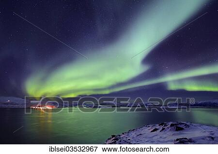 Stock Photo - "Aurora over a fjord with snow-covered mountains and an illuminated village, Tromso, â€ªTroms, Northern Norway, Norway, Europe". Fotosearch