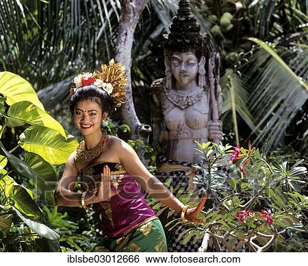 Stock Photograph - "Balinese dancer wearing a traditional costume in front of a stone statue, Candi Dasa, Bali, Sudostasien, Indonesia, Asia". Fotosearch