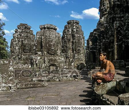 Stock Image - "Bayon temple, man sitting on the second terrace, face towers, smiling faces of Bodhisattva Lokeshvara, Avalokiteshvara, Angkor Thom, Siem Reap Province, Cambodia, Asia". Fotosearch