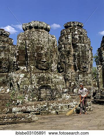Stock Image - "Bayon temple, man with broom working on the second terrace, face towers, smiling faces of Bodhisattva Lokeshvara, Avalokiteshvara, Angkor Thom, Siem Reap Province, Cambodia, Asia". Fotosearch