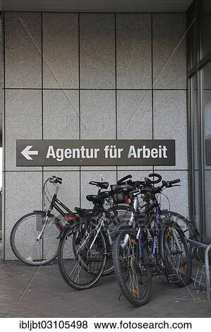 Stock Photo - "Bicycles parked in front of the sign """"Agentur fuer Arbeit"""", German for Employment Agency, Cologne, Rhineland, North Rhine-Westphalia, Germany, Europe". Fotosearch