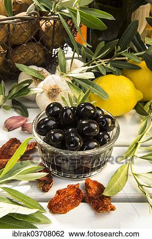 Stock Image - "Black olives in a glass bowl with lemons, garlic and olive branches, Germany, Europe". Fotosearch