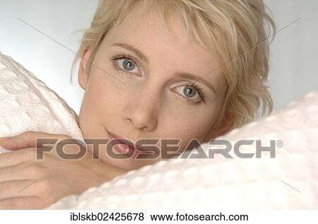 Stock Photo - "Blond woman lying between white pillows, portrait". Fotosearch