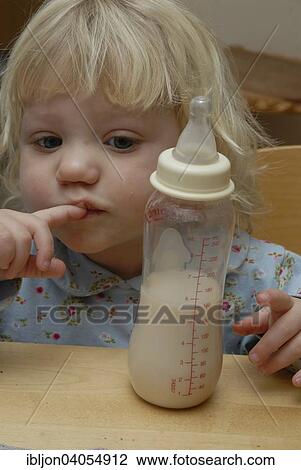 Stock Image - "Blonde girl, two years, looking at a baby bottle, Sweden, Europe". Fotosearch