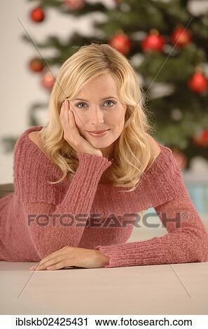Stock Image - "Blonde woman, 20-30, lying on the floor with her head propped up by her hand, Christmas ambience". Fotosearch