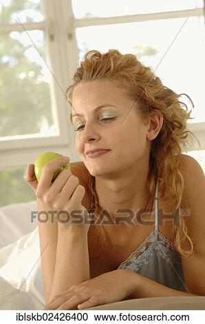 "Blonde woman, 25-35 years, is propped up on her belly in bed holding an apple" View Large Photo Image Stock Image - "Blonde woman, 25-35 years, is propped up on her belly in bed holding an apple". Fotosearch