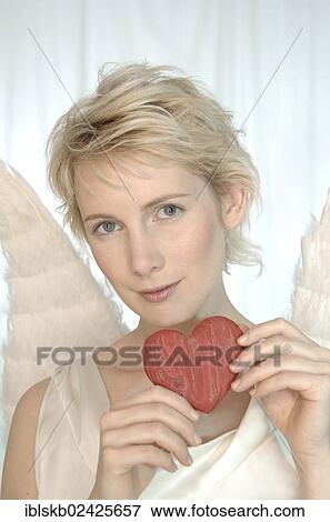 Stock Photo - "Blonde woman with angel wings, holding a wooden heart". Fotosearch