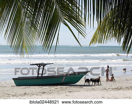 Stock Image - "Boat, Costa Rican women and dogs on the beach, Playa Samara, Nicoya Peninsula, Costa Rica, Central America, North America". Fotosearch