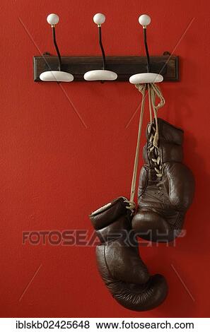 Stock Photo - Boxing gloves hanging on nostalgic coat hooks on a red wall. Fotosearch
