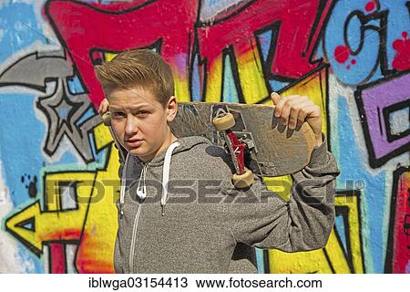 "Boy, 13 years, holding a skateboard in front of graffiti-covered wall, Germany, Europe" View Large Photo Image Stock Image - "Boy, 13 years, holding a skateboard in front of graffiti-covered wall, Germany, Europe". Fotosearch