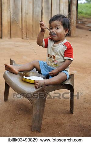 "Boy, 3, sitting on a broken chair and eating porridge, in a community of the Guarani Indians, Jaguary, Caaguazu Department, Paraguay, South America" View Large Photo Image Stock Photo - "Boy, 3, sitting on a broken chair and eating porridge, in a community of the Guarani Indians, Jaguary, Caaguazu Department, Paraguay, South America". Fotosearch