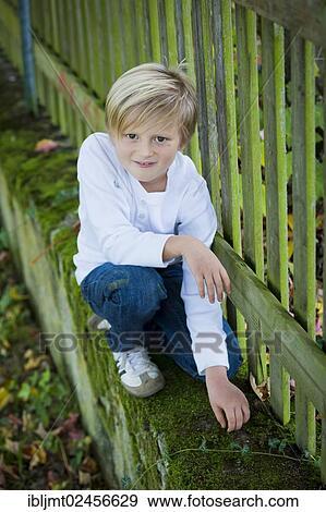 Stock Photo - "Boy, 7 years old, kneeling next to a wooden fence". Fotosearch