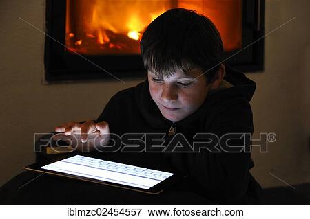 Stock Photo - "Boy, 8, using an iPad in front of a fireplace, Ringsheim, Baden-Wuerttemberg, Germany, Europe". Fotosearch