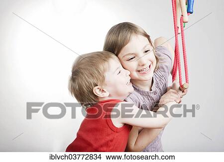 Picture - "Boy and girl, siblings, holding on tight to a swing, smiling". Fotosearch