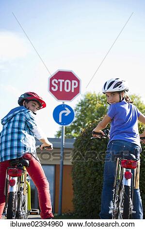 Stock Image - Boy and girl waiting with their bicycles in front of a stop sign. Fotosearch