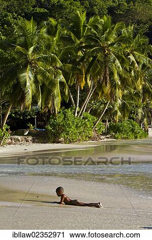 Stock Image - "Boy, Creole, lying on a sandy beach, Mahe, Seychelles, Africa, Indian Ocean, Africa". Fotosearch