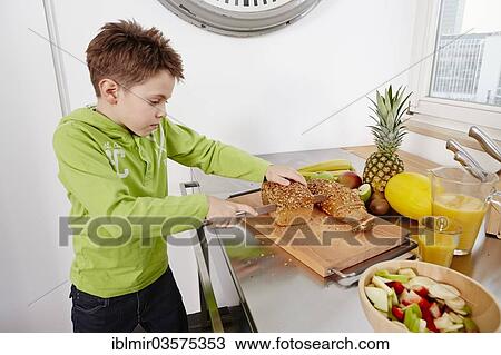 Stock Image - "Boy cutting slices off a whole wheat bread, Germany, Europe". Fotosearch