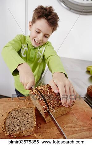 Stock Photography - "Boy cutting slices off a whole wheat bread, Germany, Europe". Fotosearch