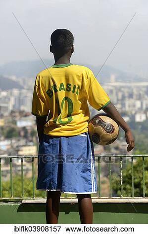 "Boy holding a soccer boy and wearing a Brazil jersey while overlooking the centre of Rio de Janeiro, Rio de Janeiro State, Brazil, South America" View Large Photo Image Stock Photo - "Boy holding a soccer boy and wearing a Brazil jersey while overlooking the centre of Rio de Janeiro, Rio de Janeiro State, Brazil, South America". Fotosearch