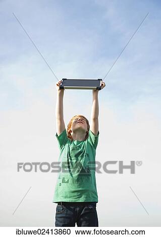 Stock Image - Boy holding a solar panel towards the sun. Fotosearch